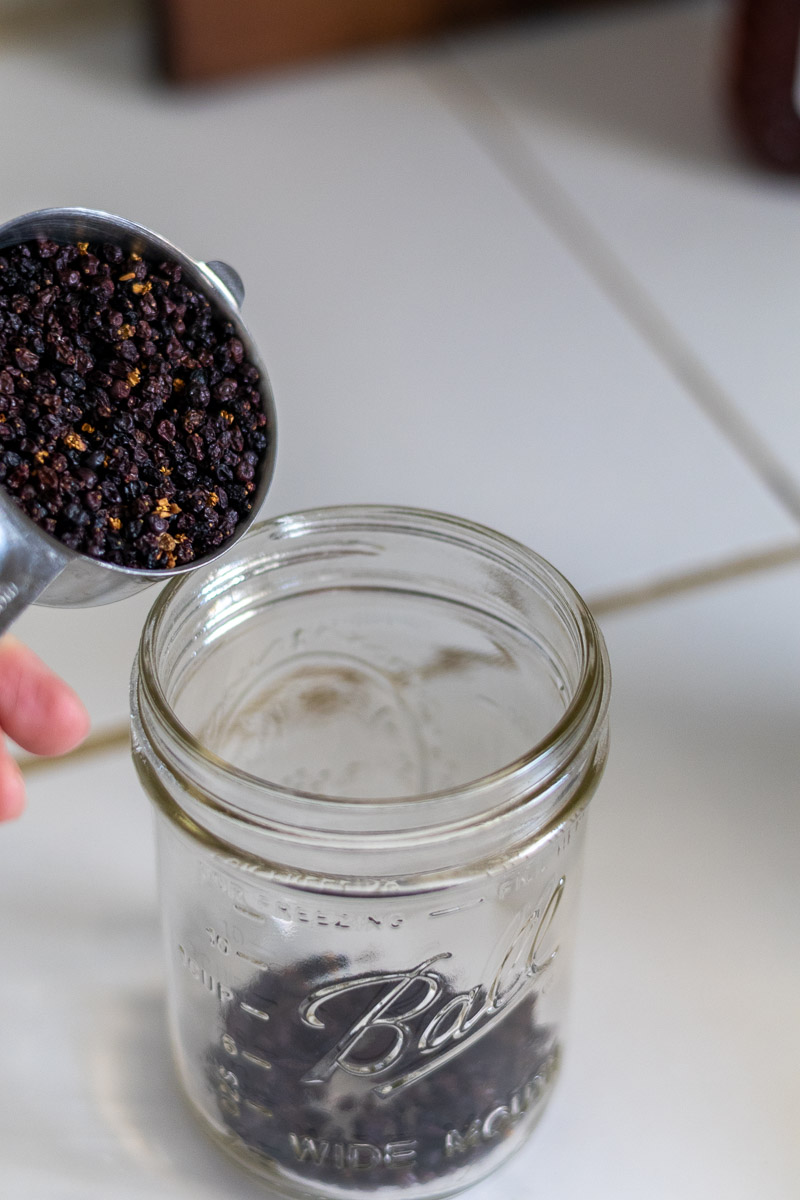 A half cup of dried elderberries being poured in a mason jar.
