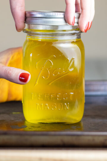 A woman's hand screwing lid on ball mason jar full of dry rendered tallow.