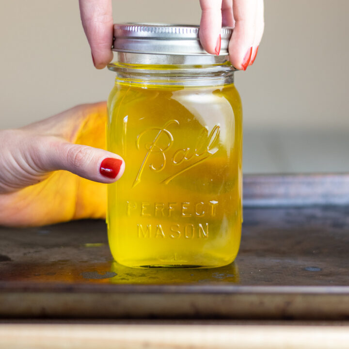 A woman's hand screwing lid on ball mason jar full of dry rendered tallow.
