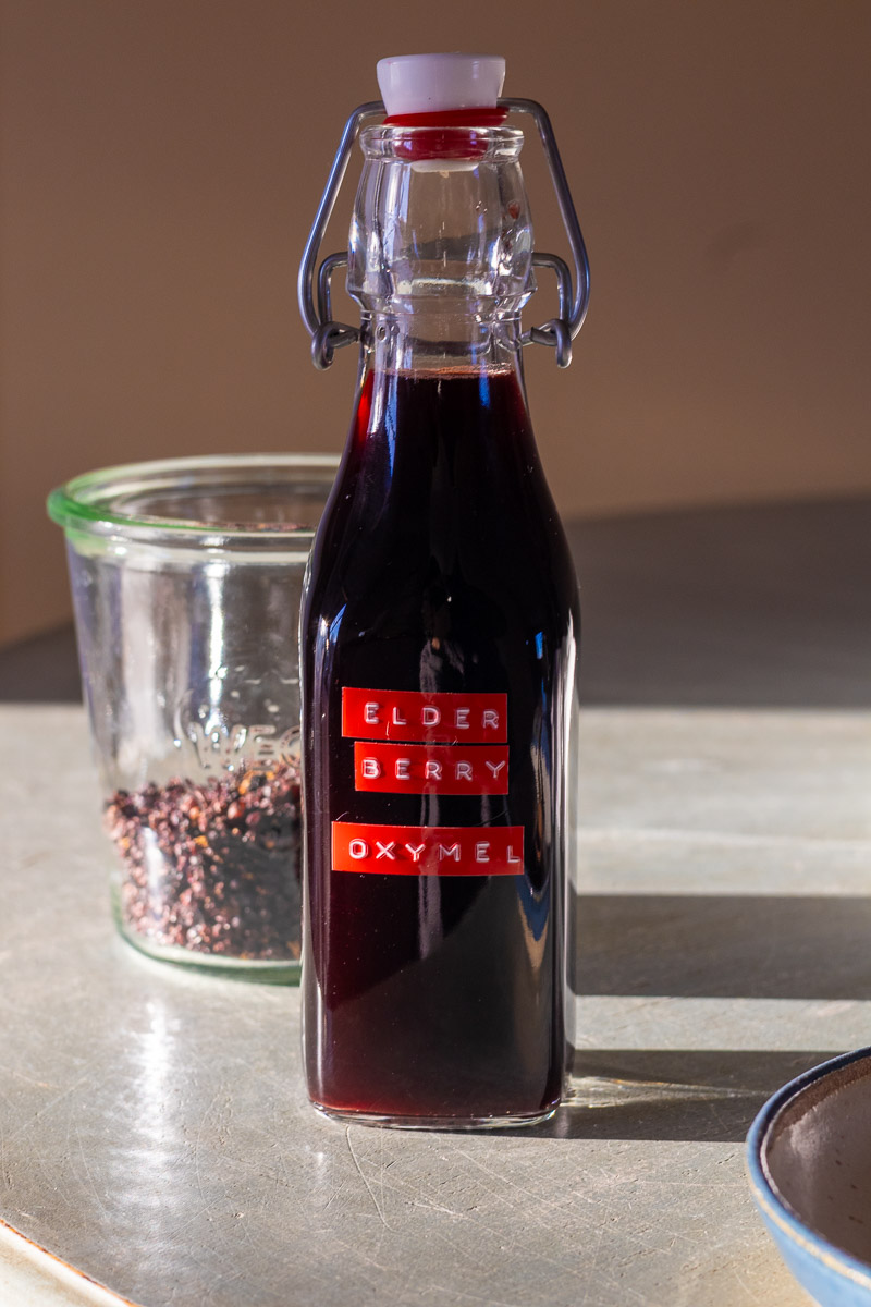 A jar of elderberry oxymel on a blue table.