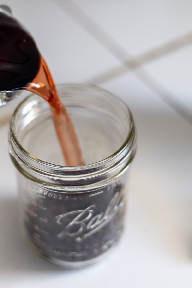 Red wine vinegar being poured into a mason jar of elderberries.