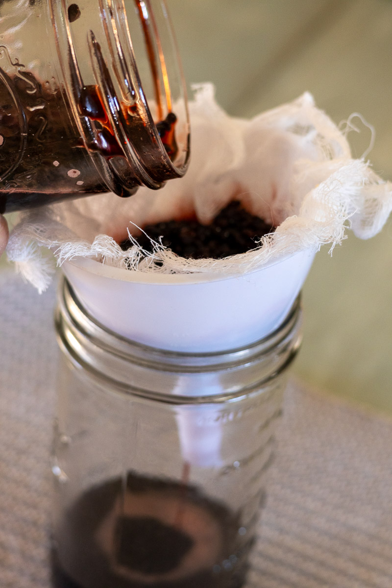 A jar, funnel, and cheesecloth straining finished elderberry oxymel.