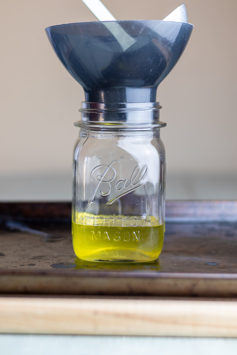 A mason jar with funnel and ladle putting tallow into that jar.