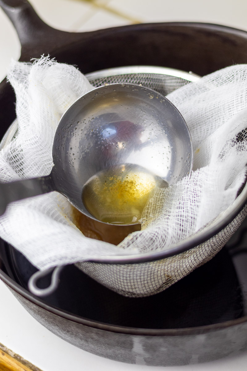 A ladle with mesh strainer and cheesecloth straining finished dry rendered tallow.