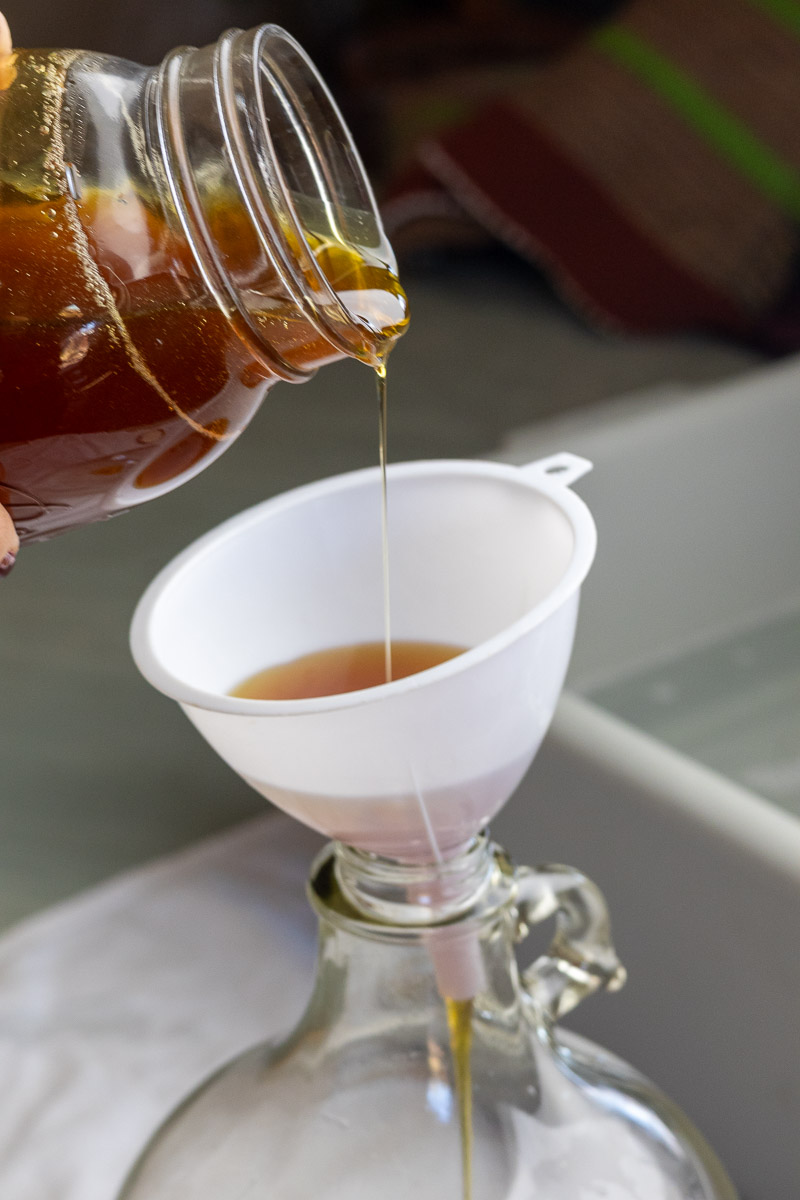 Honey being poured into a gallon carboy with white funnel.
