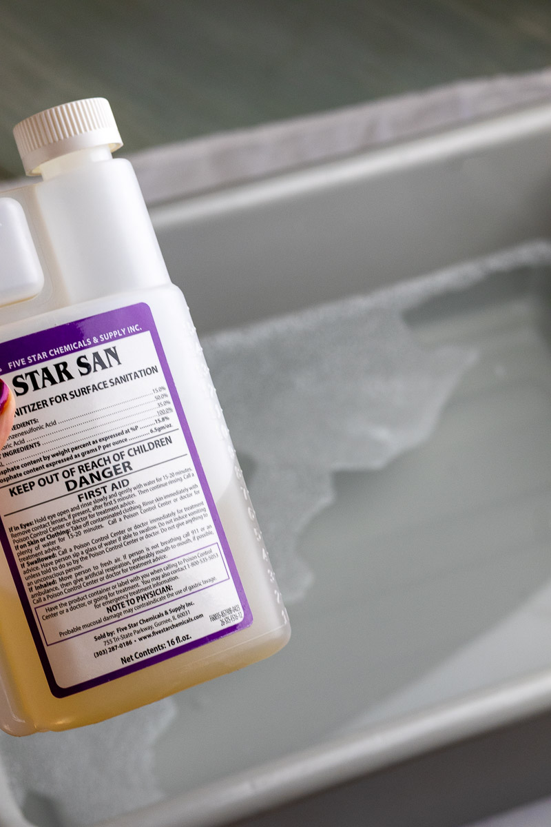 A hand showing a bottle of Star San and a bucket of sanitizing solution.