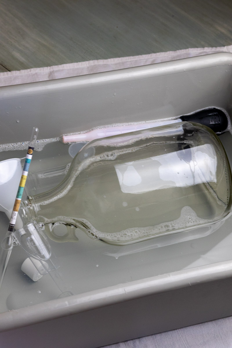 Home brewing equipment including carboy, hydrometer, and airlock in sanitizing solution.