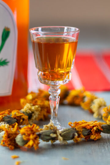 A marigold garland decorating a cordial glass with homemade liqueur inside.