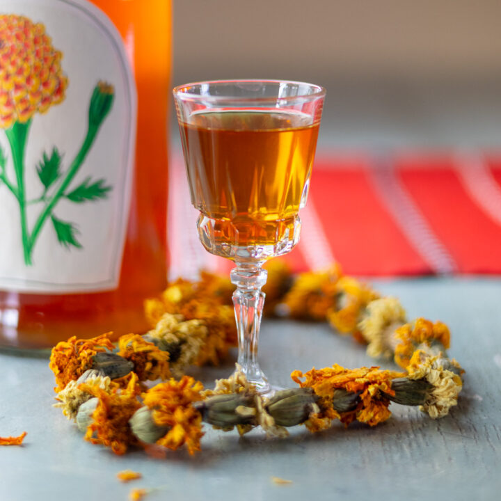 A marigold garland decorating a cordial glass with homemade liqueur inside.