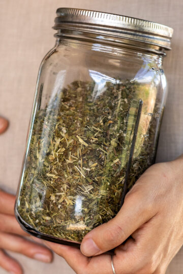 A mason jar of blended pregnancy tea blend and a woman in the background holding her belly with a hand with rings.