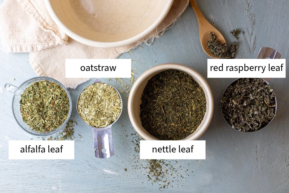 The ingredients of the pregnancy tea recipe laid out neatly on a blue table next to wooden spoon and large bowl.